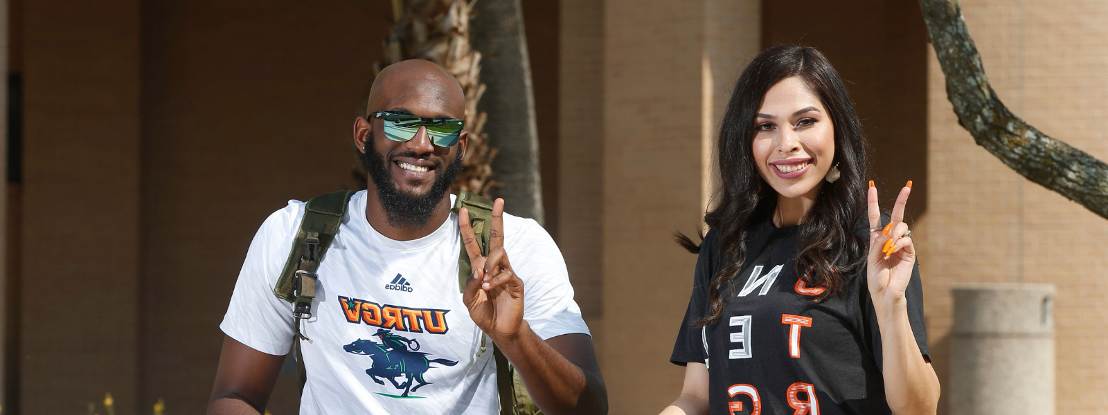 Students sitting outdoors while giving a V's up (victory hand sign.)