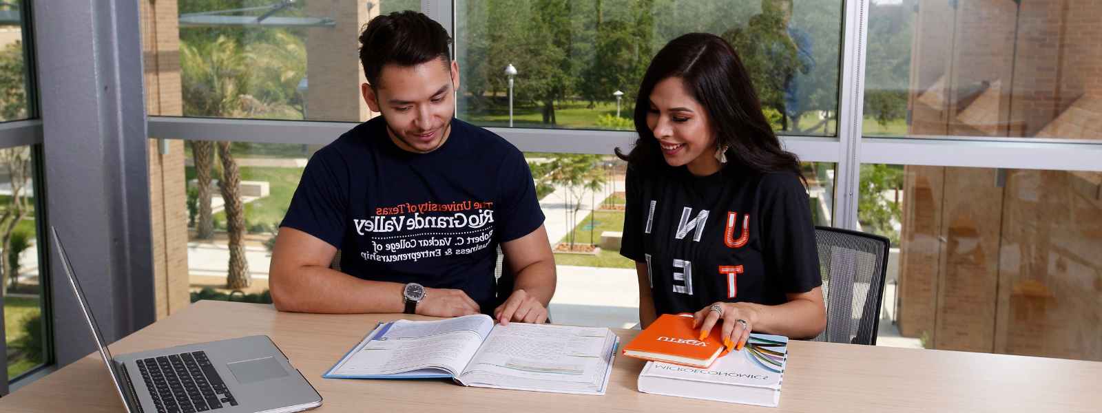 Two students studying at a desk with opened books in front of them.