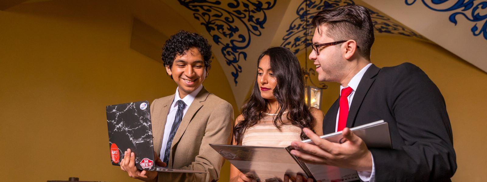 Students smile while holding documents and laptop